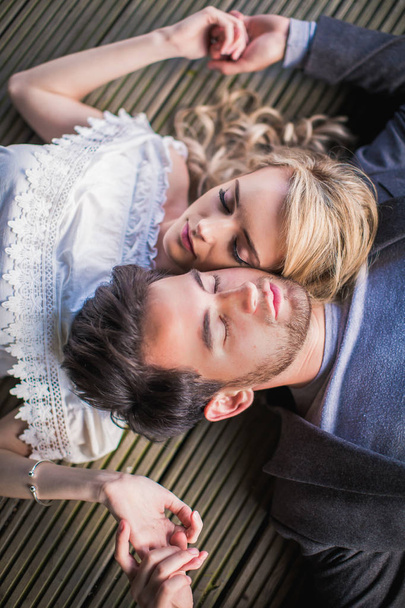 Portrait of the young charming couple in love who lying head to head with closed eyes outdoor and holding hands each other - Foto, Imagen