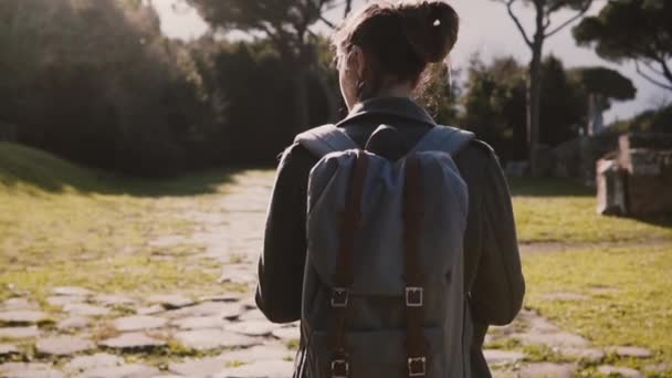 Back view of attractive travel blogger girl with backpack and map exploring ancient sunny ruins in Ostia slow motion. - Metraje, vídeo