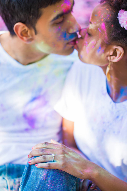 Portrait of the young couple in love with paints on their faces who sitting outdoor and kissing - Fotó, kép