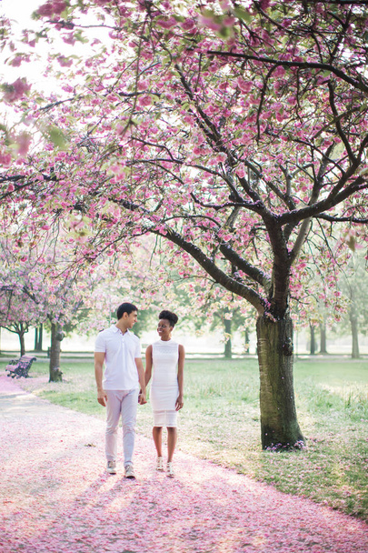 The young adorable romantic couple walking by road with petals in the park and holding hands each other - Foto, Imagem