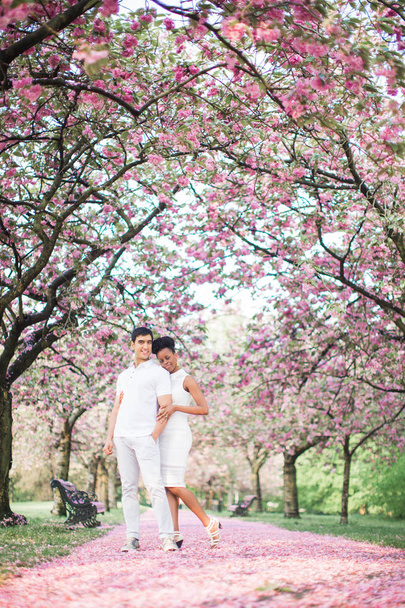 The young happy romantic couple in love standing on the road with petals in the park - Foto, Imagem