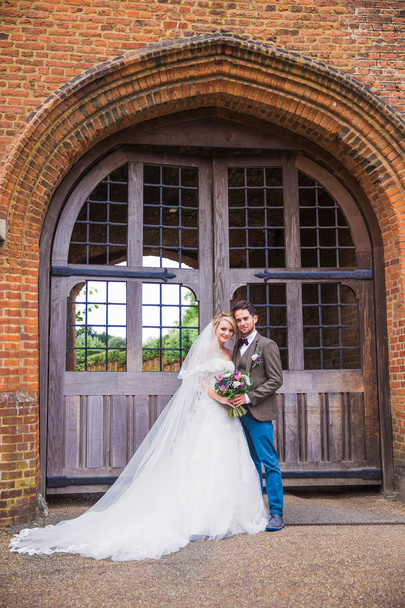 The young cheerful beautiful newlyweds standing in embrace before the door of building outdoors - Foto, immagini