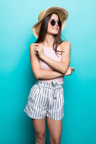Elegante junge Frau mit Sommerkleid, Strohhut und Sonnenbrille, die an ihren Sommerurlaub denkt. Seitenansicht einer Frau mit Hand am Kinn, isoliert über pastellblauem Hintergrund. - Foto, Bild