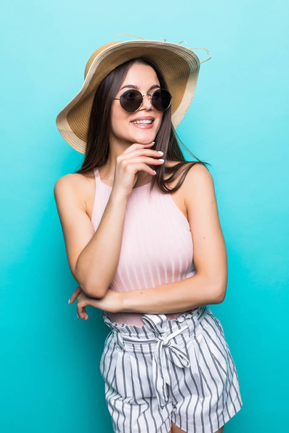 Elégante jeune femme en robe d'été, chapeau de paille et lunettes de soleil, pensant à ses vacances d'été. Vue latérale de la femme avec la main sur le menton, isolé sur fond bleu pastel
. - Photo, image