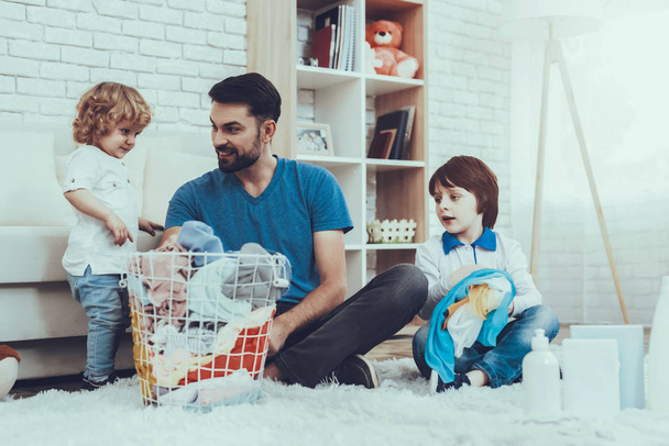 Two Boys. Help Wash Clothes. Father. Baby with Bright Hair. Smiling Kids. Spends Time. Happy Together. Leisure Time. Man. Smile. Home Time. Family. Holidays. Father Two Boys. Dirty Laundry. Basket. - 写真・画像