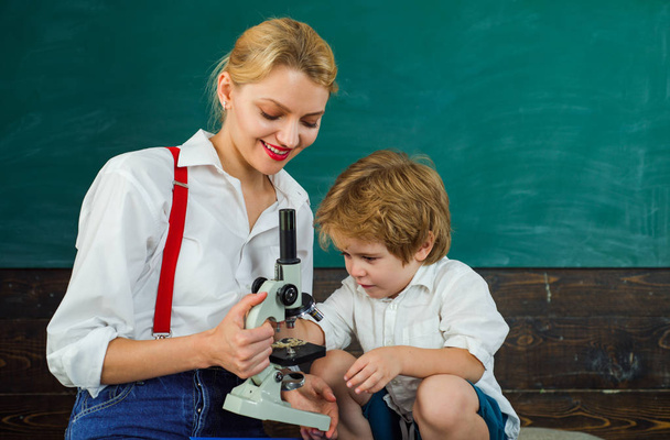 Lessons of science. Microscope. The teacher and student study biology at school. Friendly smiling teacher and pupil in classroom. Knowledge concept. Education. Teacher is warm accessible enthusiastic - Photo, Image