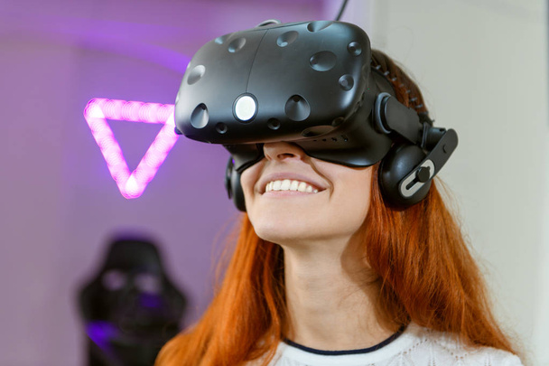 A young and very beautiful girl, with red hair, in a yellow sweater, plays games of virtual reality - Photo, Image