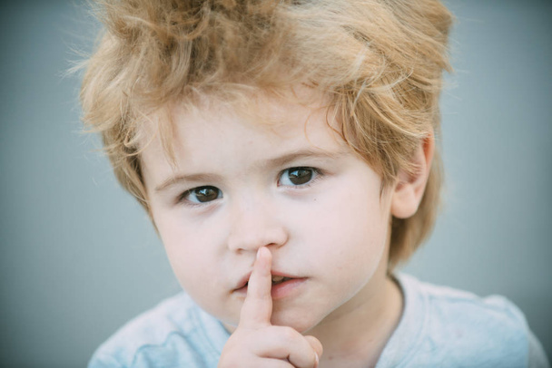 Αγόρι με το δάχτυλο στα χείλη μια σιωπηλή χειρονομία. Παρακαλώ κάνετε ησυχία. Έξυπνη χαριτωμένο νεαρό αγόρι με το δάχτυλό του πάνω από τα χείλη του being ήσυχος. Μικρό αγόρι δείχνει σιωπή σύμβολο χειρονομία. Μυστικό ο νεαρός άντρας - Φωτογραφία, εικόνα