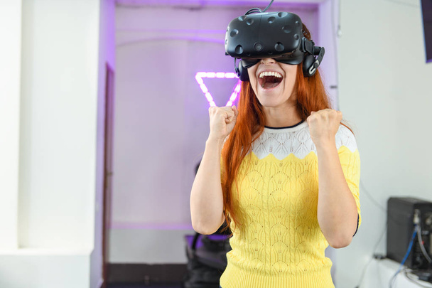 Une jeune et très belle fille, aux cheveux roux, dans un pull jaune, joue à des jeux de réalité virtuelle
 - Photo, image