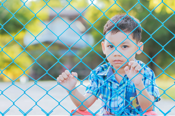 Хлопчик стоїть за парканом з емоційним виразом
. - Фото, зображення