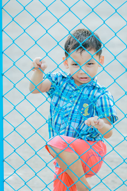 Το αγόρι που στέκεται πίσω από το φράχτη με συναισθηματική έκφραση. - Φωτογραφία, εικόνα