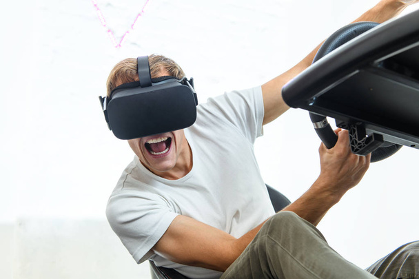 Um rapaz jovem e bonito com uma t-shirt branca, a jogar numa corrida, num simulador de realidade virtual
 - Foto, Imagem