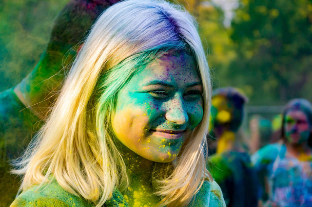 Young energetic teenagers at the festival of paints of holi in Russia. Having fun outdoors. Multicolored powder colors the face. Closeup portrait - Photo, image