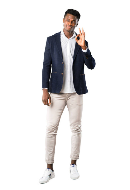 Cuerpo completo de hombre afroamericano guapo con una chaqueta que muestra un signo de ok con los dedos en el fondo blanco
 - Foto, imagen