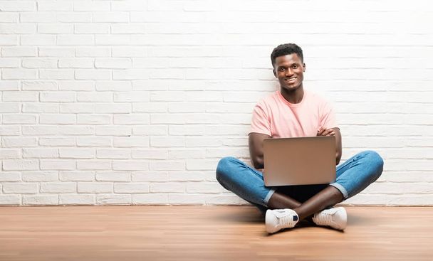 Afro-Américain assis sur le sol avec son ordinateur portable les bras croisés
 - Photo, image