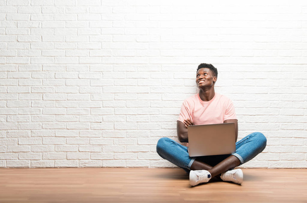 Afro american man sitting on the floor with his laptop looking up - Foto, Imagen