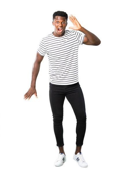 Full body of Dark skinned man with striped shirt with surprise and shocked facial expression. Gaping because can not believe what is happening on white background - Photo, Image