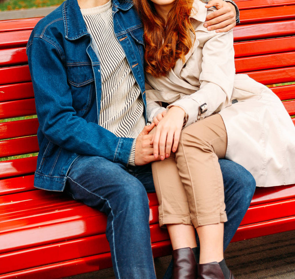 couple sitting on a bench, legs of a girl on a guy, a man hugging a woman. a guy in jeans and a denim jacket, a girl in a beige coat and pants, brown shoes - Foto, immagini