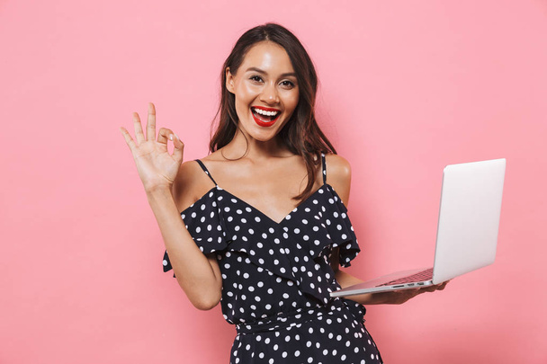Photo of happy beautiful woman isolated over pink background using laptop computer typing showing okay gesture. - Foto, afbeelding