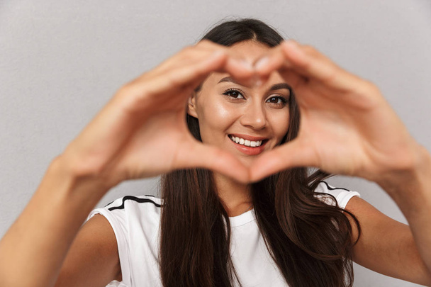 Photo of excited cheerful young woman isolated over grey background showing heart love gesture. - Foto, immagini