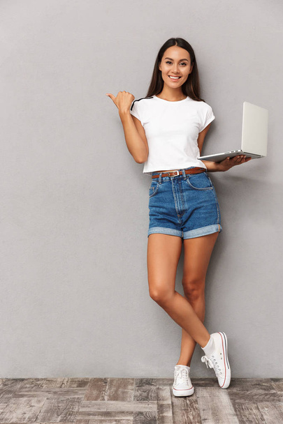 Image of happy young woman isolated over grey background using laptop computer pointing. - Fotoğraf, Görsel