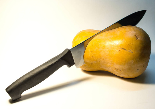 An orange pumpkin on a white background is cut with a knife.Vegetables as symbols of holidays.  - Fotografie, Obrázek