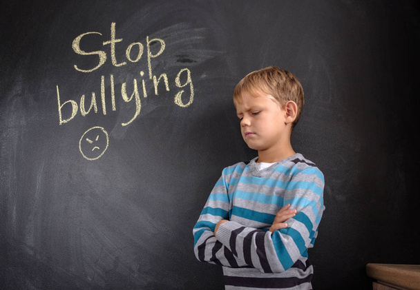 Menino perto de quadro-negro com palavras "Pare de bullying" dentro de casa
 - Foto, Imagem