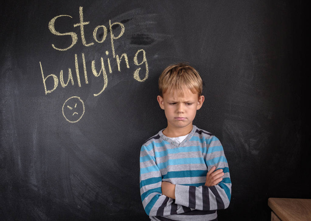 Маленький мальчик возле доски со словами "Хватит издеваться" в помещении
 - Фото, изображение