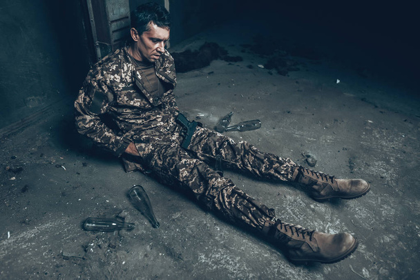 Man Is Sitting In War Shelter With Shotgun. Camouflage Uniform. Military Actions. War Hideaway Concept. Bottle With Alcohol. Occupation Problem. Depressed Soldier. Disappointed Hero. - Foto, immagini