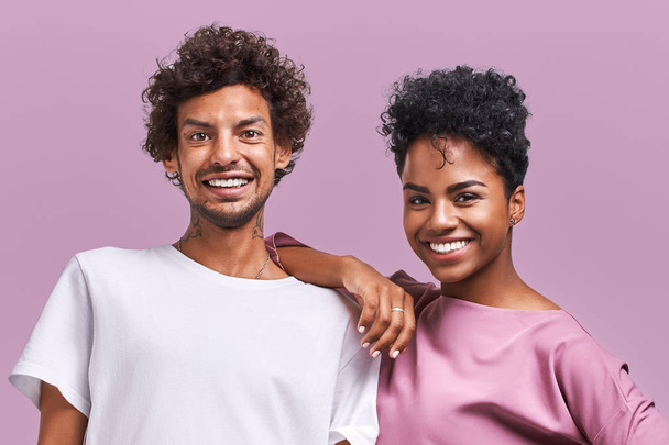 Joyful dark skinned female and male fellows have pleasant smiles on faces, satisfied after outdoor training, spend free time together, isolated over pink background. Ethnicity and friendship concept - Zdjęcie, obraz