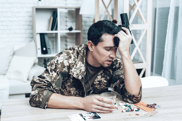 A Man In Camouflage At Home With Shotgun. Depression After War Concept. Sad Homecoming. Returning From Army. Posttraumatic Disorder. Painful Memories. Photo From War. Glass Of Whiskey. - 写真・画像