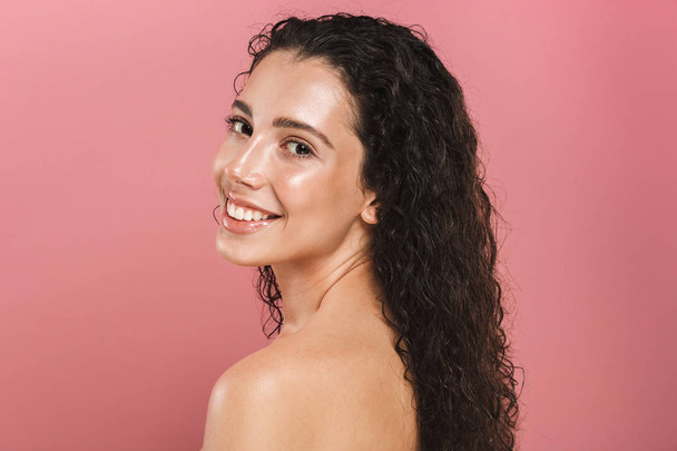 Beauty portrait of a smiling young topless woman with curly brunette hair posing over pink background - Фото, изображение