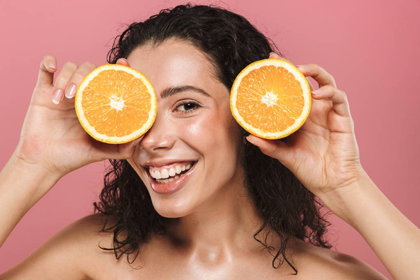 Beauty image of european half naked woman with long hair smiling and holding pieces of orange isolated over pink background - Fotoğraf, Görsel