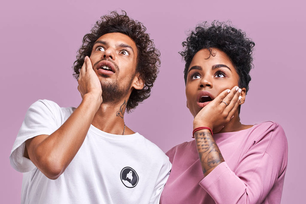 Wow, what is on floor Surprised young dark skinned male and female couple keep hands on cheeks, looking up with amazed face expressions how grew their bills, pose against lavender background - Valokuva, kuva