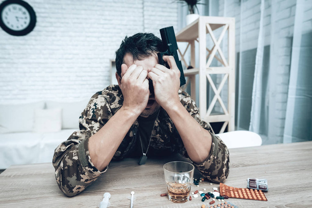 A Man In Camouflage At Home With Shotgun. Depression After War Concept. Sad Homecoming. Returning From Army. Posttraumatic Disorder. Painful Memories. Photo From War. Glass Of Whiskey. - Photo, image