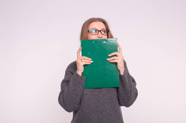 Smart young blonde woman in glasses hiding behind green paper folder. - Photo, image