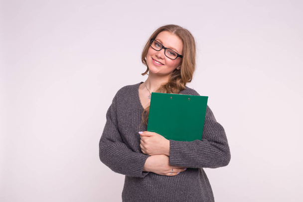 Portrait of calm smart young woman holding green paper folder on white background - Photo, Image
