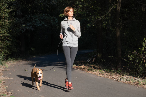 Woman jogging with dog in a park. Young female person with pet doing running exercise in the forest - Foto, Imagen