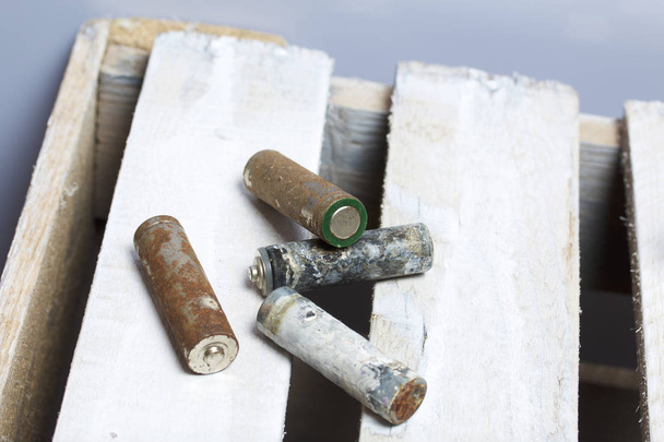 Used finger-wound batteries covered with corrosion. They lie on a wooden box. Recycling. - Foto, imagen