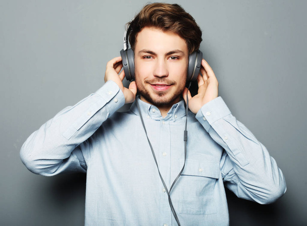 life style, happiness, emotional and people concept: Enjoying his favorite music. Happy young stylish man adjusting his headphones ad smiling - Фото, зображення