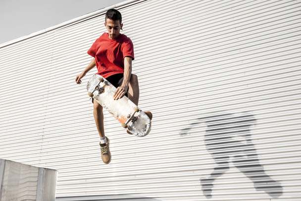 young skateboarder jumps up with his board in front of a metal background on the roofs of an abandoned building - Foto, Bild