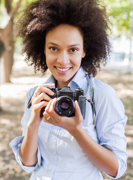 Portrait de charmante femme noire avec appareil photo rétro, photographe femme en plein air, coiffure afro, porte des vêtements décontractés, regardant la caméra
 - Photo, image