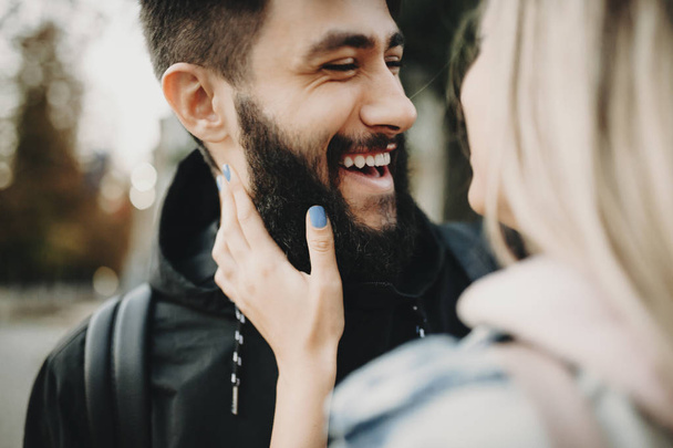 Hombre barbudo alegre con la mujer riendo felizmente mientras se abraza en la calle y se mira entre sí
 - Foto, imagen