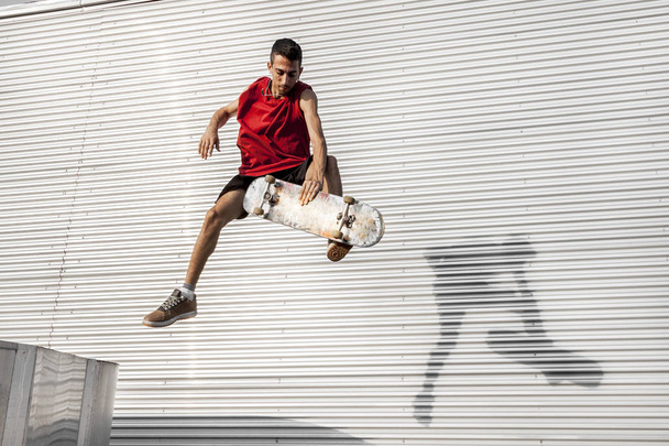 young skateboarder jumps up with his board in front of a metal background on the roofs of an abandoned building - Fotoğraf, Görsel