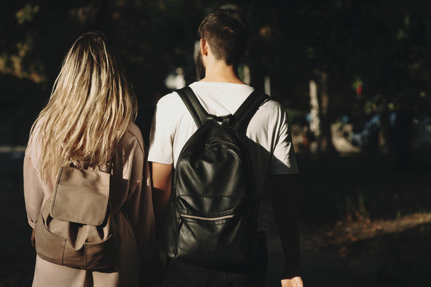 Back view of man and woman wearing backpacks and standing together in sunny park - Photo, Image