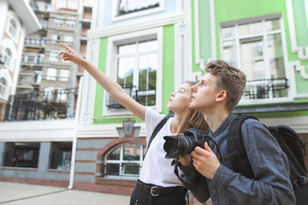 Jonge paar toeristen lopen rond de oude stad, een aantrekkelijk meisje toont een hand, dat een jonge man met een camera in zijn handen kijkt naar de kant. Mooie jonge paar reizen. - Foto, afbeelding