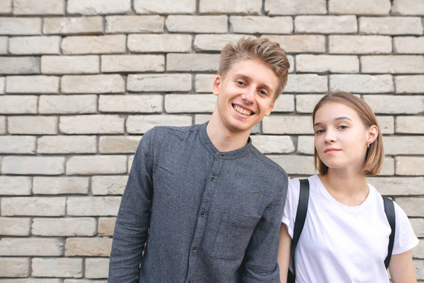 Beautiful young couple, boy and girl standing against a brick wall, smiling and looking at camera. Love Story. Copyspace - Photo, image