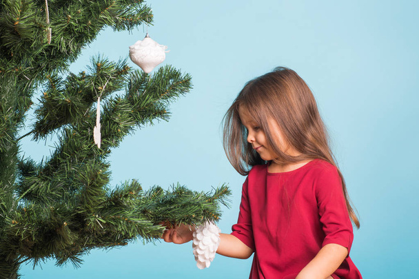 Christmas, childhood and people concept - little girl decorating the christmas tree - Foto, Bild