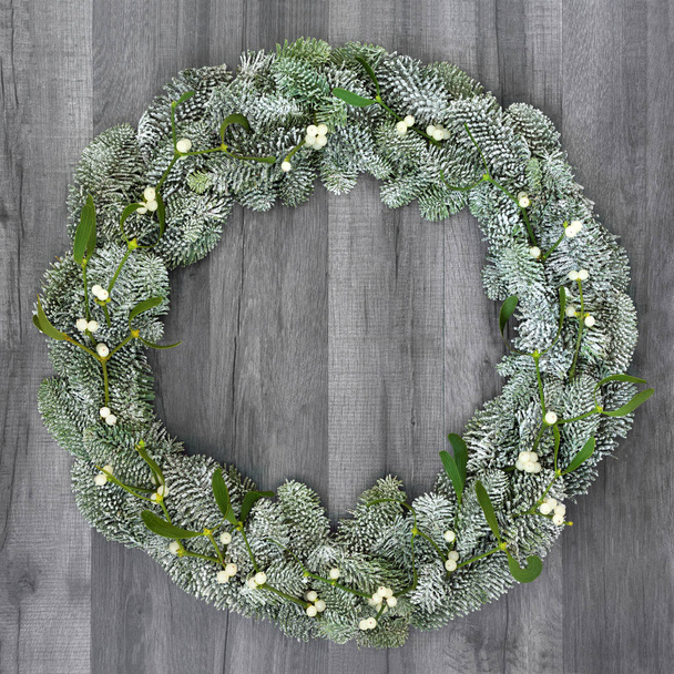 Corona de invierno y Navidad con muérdago y abeto cubierto de nieve abeto sobre madera gris rústica
. - Foto, Imagen
