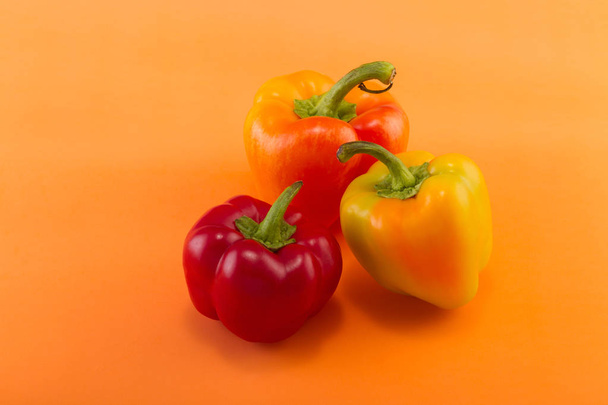 Sweet bellpepper. Two orange-yellow and one red sweet bellpeppers on an orange background. Three pieces. Studio light. Top view - 写真・画像